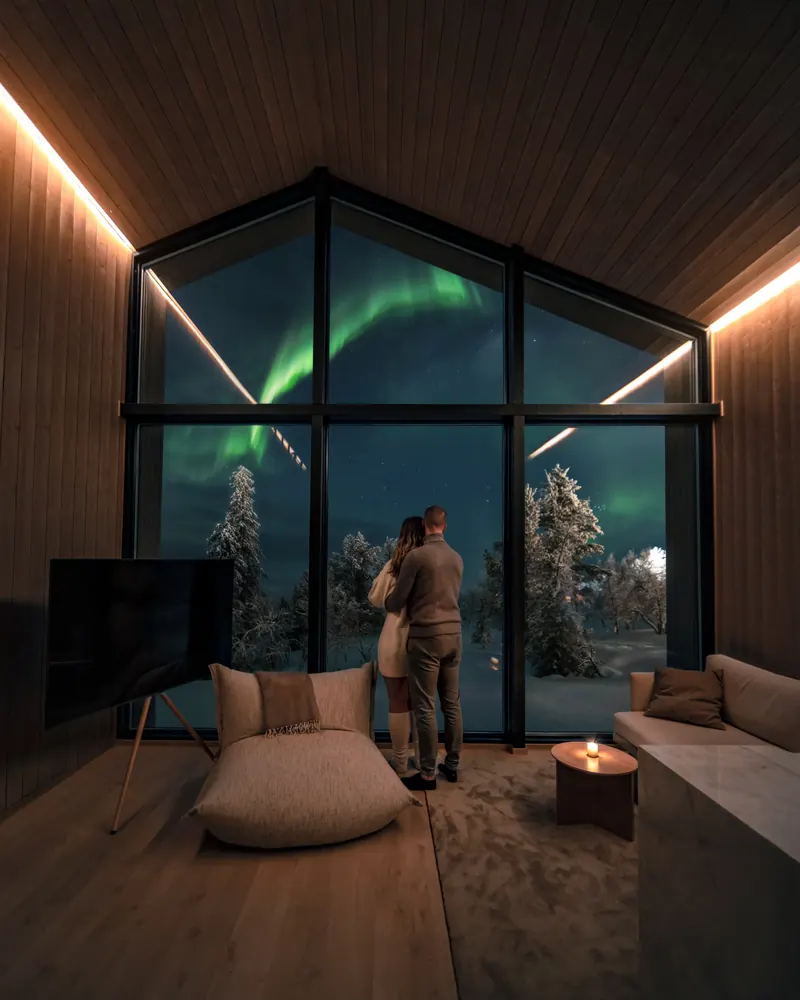 A couple watching the northern lights through a cabin’s glass wall